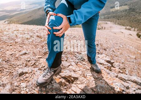 La donna si sta trattenendo sull'articolazione del ginocchio, soffrendo di dolore acuto. Concetto di lesione del menisco durante un'escursione nelle alture Foto Stock