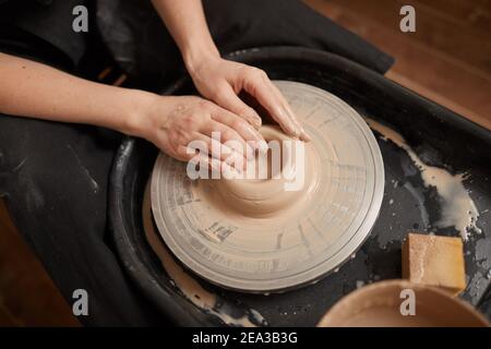 Alto angolo di primo piano di eleganti mani femminili che modellano l'argilla sulla ruota in ceramica in officina, spazio di copia Foto Stock