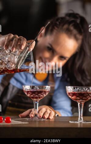 Il barista femminile versa il cocktail manhattan in un bicchiere ornamentale. Foto Stock