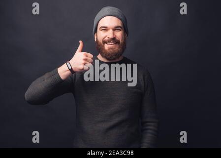 Ritratto di bell'uomo bearded che mostra il pollice su sfondo nero. Foto Stock