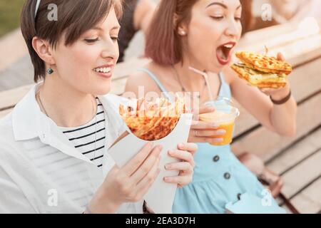 Due felici amici donne che si rilassano nel parco cittadino e mangiano cucina moderna di strada. Dieta sana e vacanza fastfood urbano Foto Stock