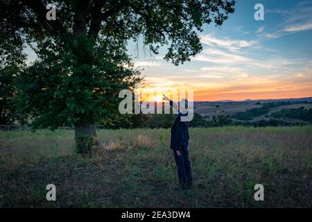 Botanico senior che parla con l'albero magico al tramonto Foto Stock
