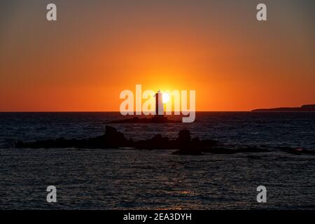 Il Sole si trova alle spalle del Faro di Mangiabarca di fronte a Carloforte, Isola di San Pietro, e Calasetta, Sant'Antioco Foto Stock