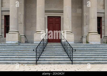 Sei grandi colonne rotonde in cemento in cima a scalini di marmo con binari in ferro nero per un edificio legale. L'edificio governativo ha un'alta porta rossa. Foto Stock