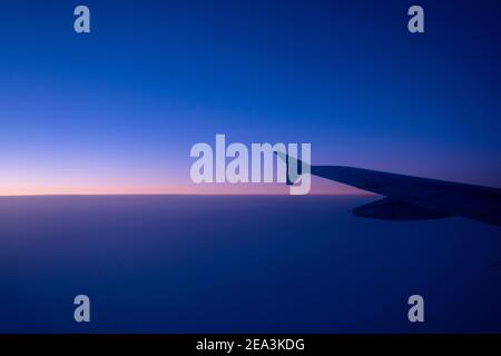 L'ala sinistra di un grande aereo commerciale bianco che sorvola l'Oceano Atlantico sotto il sole del mattino. Foto Stock