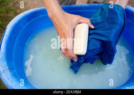 Lavaggio manuale delle mani. Primo piano di lavanda donna lavanderia in plastica blu bacino esterno. Le mani femminili lavano i vestiti in wate saponato Foto Stock