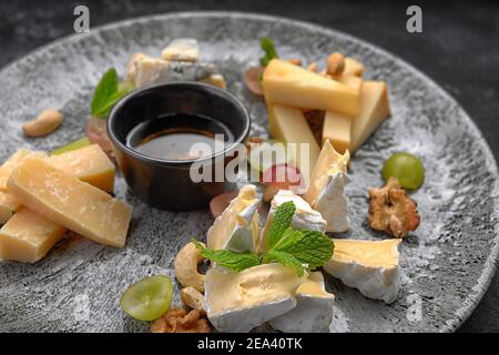 Piatto di formaggi, formaggi assortiti alla menta, frutta candita, miele e biscotti, su un piatto, su fondo scuro Foto Stock