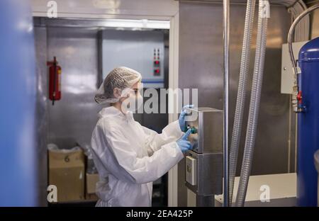 Vista laterale ritratto della giovane operatrice premendo i pulsanti sul pannello di controllo mentre si utilizzano le macchine in fabbrica alimentare, copia spazio Foto Stock