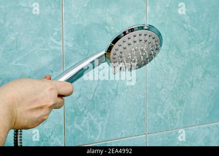 Getti d'acqua corrono dal soffione della doccia tenuto dalla donna in mano. Foto Stock