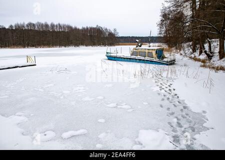 Una grande barca intrappolata nel ghiaccio su un lago. Un lago ghiacciato in un molo. Stagione invernale. Foto Stock