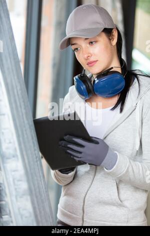 lavoratore manuale femminile con cuffie antirumore che utilizzano un tablet digitale Foto Stock