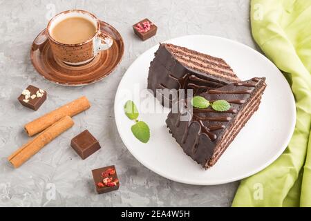 Torta al cioccolato fatta in casa con crema di latte e una tazza di caffè su fondo grigio in cemento con tessuto verde. Vista laterale, primo piano. Foto Stock