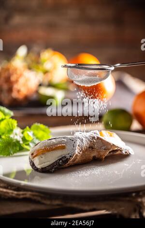 Dolce siciliano di Cannoli condito con zucchero su sfondo rustico. Foto Stock