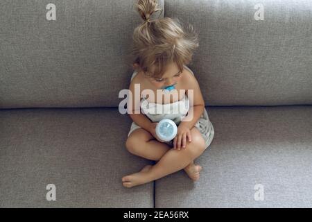 Cute Little Baby con piacere trascorrere il tempo a casa. Seduta sul lettino per preparare un pasto. Formula del latte del bambino. Nutrizione biologica sana dei bambini. Foto Stock