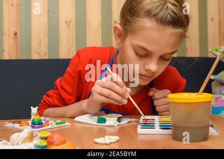 Una ragazza si tuffa un pennello in vernice del desiderato colorare mentre dipinge un mestiere da pasta di sale Foto Stock