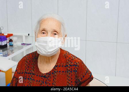 Ritratto di una donna anziana in una maschera medica. Donna anziana in un ufficio medico Foto Stock