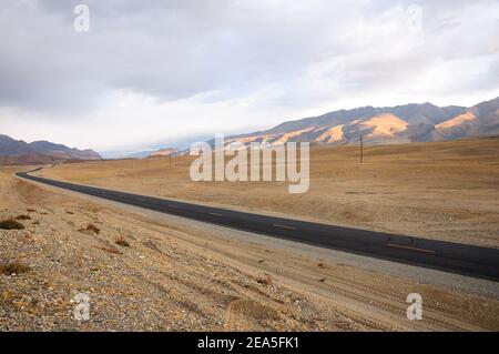 Nuova strada asfaltata a due corsie che corre lungo la linea elettrica attraverso la steppa autunnale circondata da montagne al mattino presto. Tratto di Chuisky, Altai, S. Foto Stock