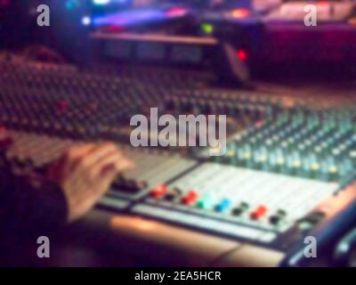 Console mixer Blurred Sound ENGINEER in concerto in interni. Mano di un tecnico del suono sfocato che usa il cursore del mixer audio che lavora in scena mostra le prestazioni. Foto Stock