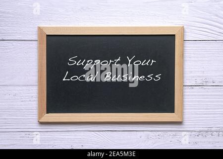 Sostenere il vostro commercio locale, parole scritte sulla lavagna. Promemoria per sostenere e acquistare beni e servizi nella tua comunità. Foto Stock