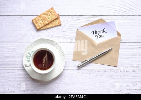 Grazie carta all'interno busta marrone accanto a tazza di tè, biscotti e penna. Vista dall'alto. Foto Stock