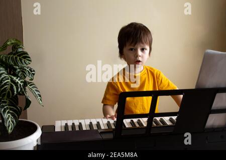 Un ragazzo che suona il sintetizzatore. Bambino imparando a suonare il pianoforte. Bambino che guarda la fotocamera. Sviluppo precoce e concetto di istruzione Foto Stock