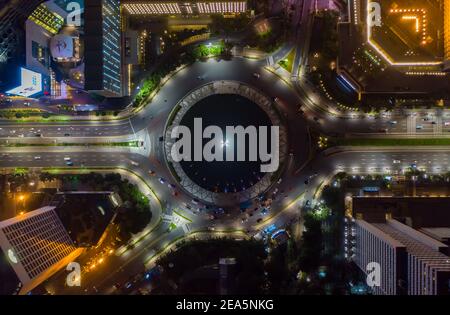 Vista aerea dall'alto del traffico di auto in movimento alla rotatoria del traffico stradale intorno al monumento Selamat Datang a Giacarta, Indonesia di notte Foto Stock