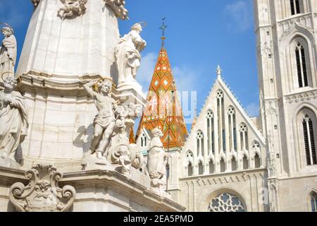 La pietra bianca e le statue e le sculture in marmo sul Statua della Santissima Trinità a Budapest Ungheria con la guglia e. Facciata della Chiesa di Mattia dietro Foto Stock