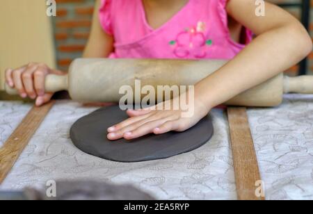 Una giovane ragazza asiatica carina imparando a modellare l'argilla nella sua classe di ceramica, modellando l'argilla in un piatto e decorandola. Foto Stock