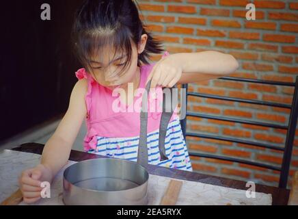 Una ragazza asiatica carina nella sua classe di ceramica, sta tagliando e stampando la sua argilla in un piatto. Foto Stock