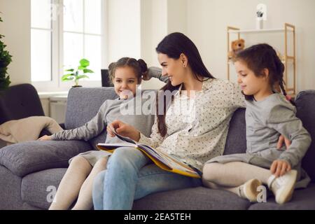 Madre con le sue figlie piccole gemelle stanno leggendo fiabe e guardando le immagini in un libro. Foto Stock