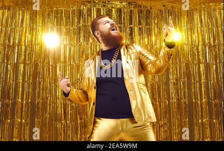 Felice eccitato uomo chubby bearded in divertente vestito d'oro lucido divertirsi in discoteca Foto Stock