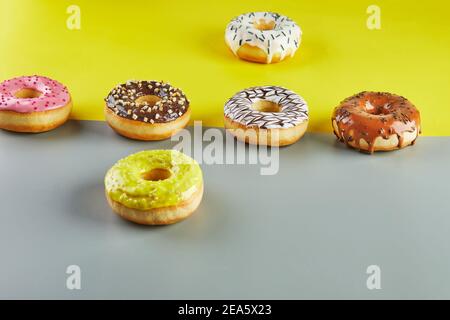 Ciambelle multicolore con smalto e spruzzate su sfondo giallo-grigio Foto Stock