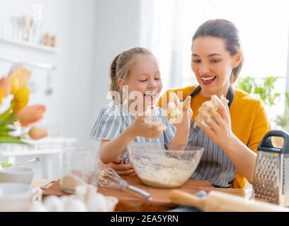 La famiglia amorosa felice sta preparando insieme la panetteria. Madre e bambina bambina ragazza stanno cucinando biscotti e divertirsi in cucina. Cibo fatto in casa e. Foto Stock