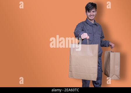 Uomo di consegna con borse di carta in mano che consegna l'ordine, vestito in uniforme e sorridente Foto Stock