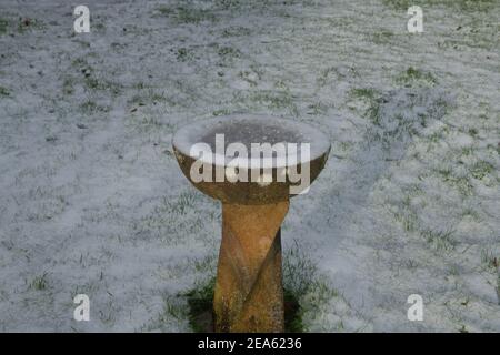 Acqua congelata in un bagno di uccello di pietra circondato da neve in un giardino rurale in Devon rurale, Inghilterra, Regno Unito Foto Stock