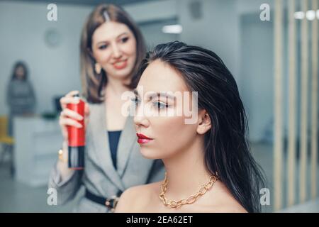 Una ragazza parrucchiere e stilista mette i capelli spray su un giovane cliente in un salone di bellezza Foto Stock