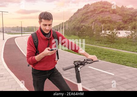 giovane uomo in libri di abbigliamento casual e paga per un condiviso scooter elettrico in affitto su una strada della città Foto Stock