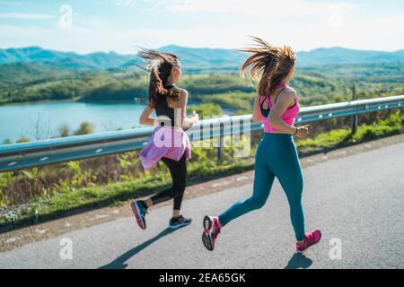 Ragazze con lunghi capelli ondulati che corrono felici lungo il lago e verdi colline Foto Stock