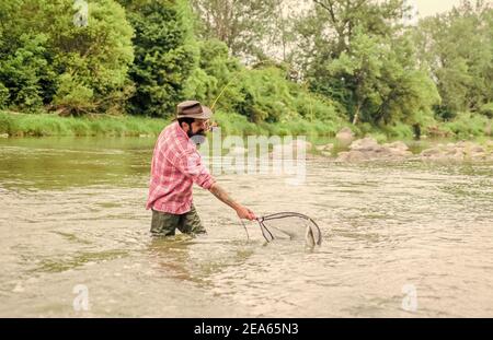 Hobby di pesca. pescatore brutale bearded che cattura il pesce di trota con la rete. Se pesce regolarmente sapete come ricompensare e calmante pesca è. La pesca è uno sport all'aperto accessibile con sedia a rotelle. Foto Stock