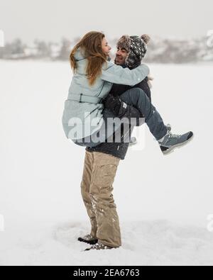 Giovane coppia felice a piedi nel giorno d'inverno. Uomo sollevando la donna Foto Stock
