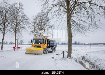 Pala gommosa da neve che discibano una strada rurale mentre si sparge il sale Nei Paesi Bassi Foto Stock