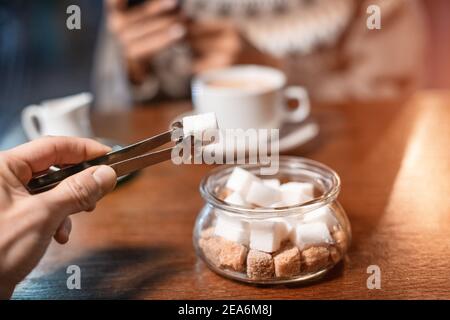 Un amante del caffè addicted mette un pezzo di zucchero bianco nella sua bevanda calda nel caffè. Concetto di dieta malsana e diabete Foto Stock