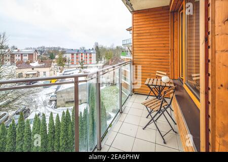 Tavolo e sedie in legno sul balcone in un moderno appartamento di lusso. Vista sulla città invernale con alberi verdi. Foto Stock