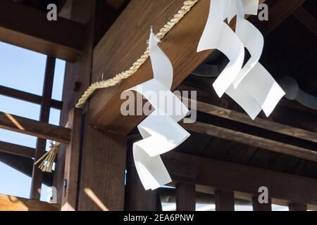 Due scalatori di carta bianchi a forma di zig-zag, usati per la purificazione e la benedizione nelle cerimonie di Shinto, appesi ad un ingresso del santuario a Nara, Giappone Foto Stock