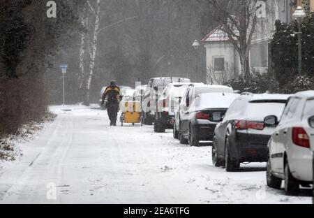 Berlino, Germania. 8 febbraio 2021. Un postino cammina verso la sua cargo bike su una strada innevata a Tempelhof. Neve e freddo gelido continuano a dominare il tempo. Credit: Bernd von Jutrczenka/dpa/Alamy Live News Foto Stock