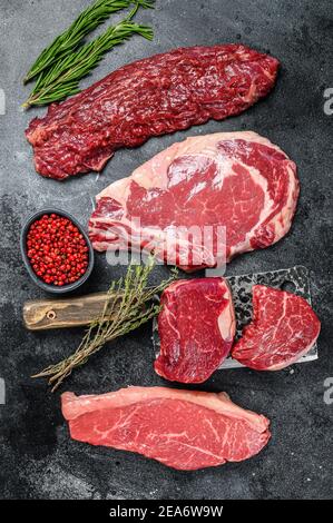 Varietà di manzo nero grezzo angus filetto di manzo Mignon, ribeye, Striploin e gonna o machete. Sfondo scuro. Vista dall'alto Foto Stock