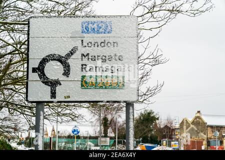 Parzialmente coperto di neve, cartello stradale britannico che mostra una rotatoria e il percorso per la M2 Londra, e poi Ramsgate e Margate dalla A299. Foto Stock