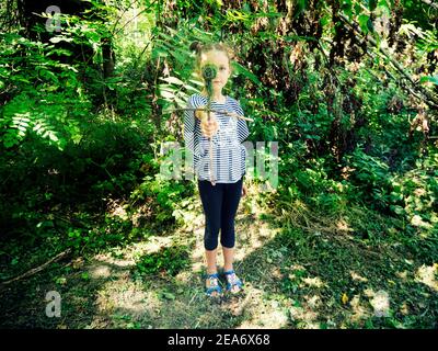 Ragazza in piedi nei boschi che tiene una bambola fatta di rami e foglie, Ungheria Foto Stock