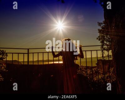 Silhouette di una ragazza che guarda una vista lago da un balcone al tramonto, Italia Foto Stock