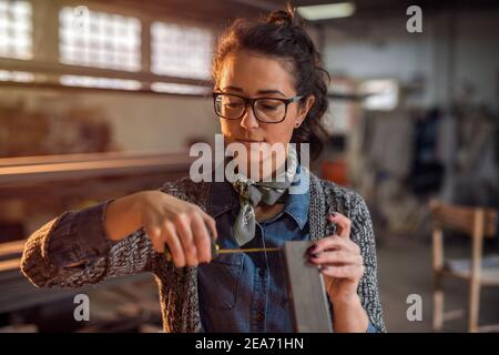 Giovane ingegnere industriale femminile che prende misure di tubo metallico nella sua officina. Foto Stock